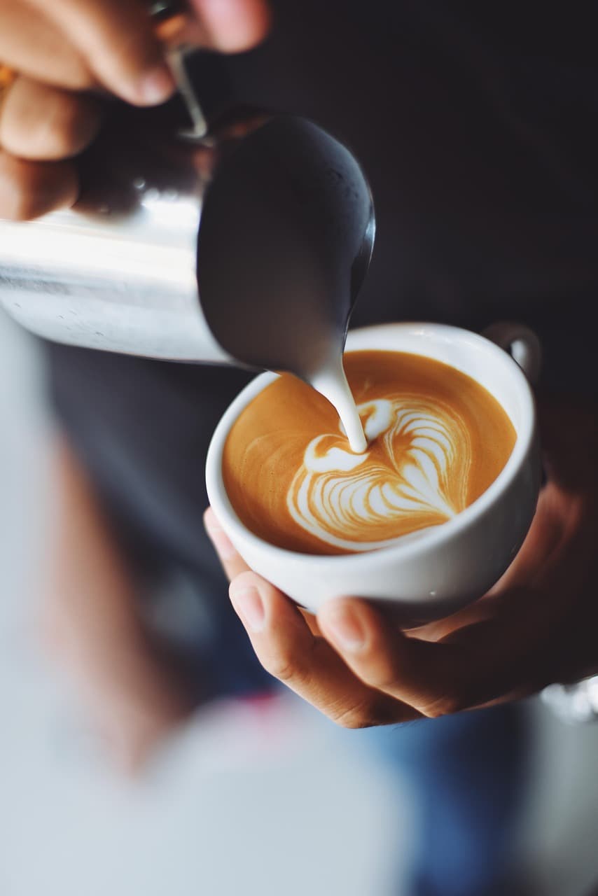 Barista pouring latte art into a white cup